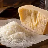 Un pezzo di Parmigiano Reggiano accanto a una montagnetta di formaggio grattugiato. Si può congelare il parmigiano grattugiato per averlo sempre pronto.