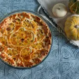 Torta salata zucca salsiccia e stracchino, con decorazione a intreccio e ripieno dorato. Accanto, zucche decorative.