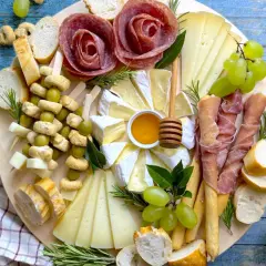Un vassoio con formaggi, salumi a rosa, uva, olive e pane. Ecco come disporre i salumi nel piatto per un antipasto invitante.