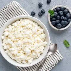 Ricotta più magra in una ciotola bianca, con mirtilli freschi e foglie di menta. Un cucchiaio d'argento è accanto.