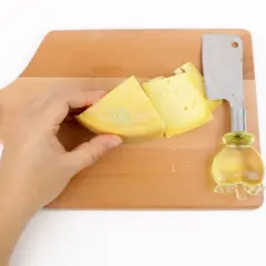 Mano che tiene un pezzo di formaggio giallo su un tagliere di legno, pronto per imparare come tagliare il formaggio a spicchi con un coltello.