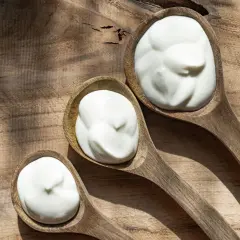 Tre cucchiai di legno pieni di panna da cucina, su un tagliere rustico.