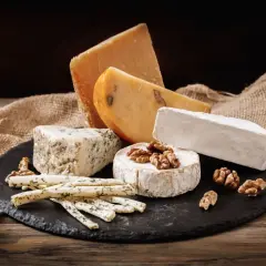 Selezione di formaggi su tagliere di ardesia: brie, erborinato, stagionato e grissini alle erbe. Un'idea per una dieta equilibrata e gustosa.