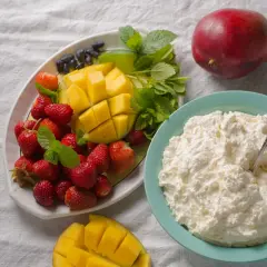 Un piatto di fragole, mango e mirtilli accanto a una ciotola di cosa sono i fiocchi di latte, con un mango intero sullo sfondo.
