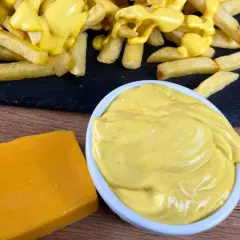 Patatine fritte ricoperte di cremosa salsa cheddar, con un blocco di formaggio e una ciotola di salsa a lato.