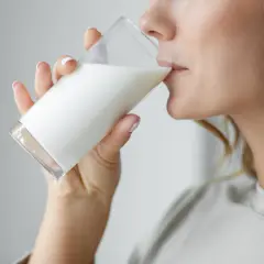 Donna bionda beve un bicchiere di latte. C'è chi dice che il latte fa ingrassare, ma lei sembra goderselo.