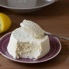 Ricotta fresca su piatto viola, con limone e cucchiaino. Perfetta per ogni ricetta.
