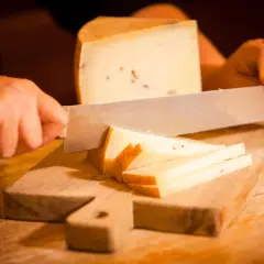 Mani che tagliano formaggio su un tagliere di legno. Fette sottili e un pezzo più grande di formaggio stagionato.