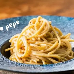 Un piatto di spaghetti fumanti, conditi con una cremosa salsa cacio e pepe, serviti in un piatto blu decorato.