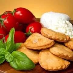 Panzerotti pugliesi dorati, pomodorini freschi, mozzarella a cubetti e basilico profumato su un tagliere di legno.