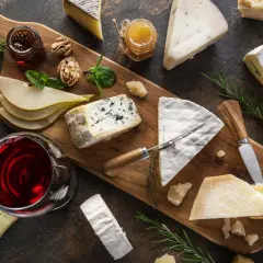Tagliere con vari formaggi, tra cui un formaggio inglese, pere, noci, miele e vino rosso.