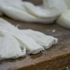 Formaggio a pasta filata, lavorato a mano, con fili bianchi e morbidi su un tagliere di legno.