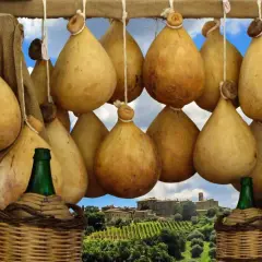 Formaggio cacio appeso, con sfondo di un borgo toscano e vigneti.