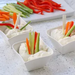 Tre ciotoline con mousse di caprino e bastoncini di verdure fresche: carote, cetrioli e peperoni rossi.