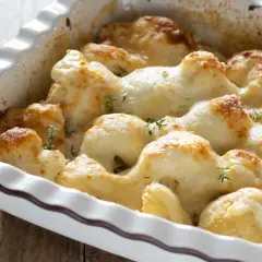 Cavolfiore al forno con pangrattato e formaggio filante, guarnito con rametti di timo fresco.