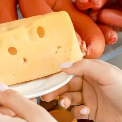 Mano prende un pezzo di formaggio svizzero da un frigorifero pieno di salumi. Formaggi salutari per uno spuntino.