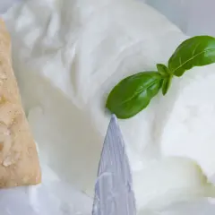 Un panino integrale con semi e un blocco di cremoso stracchino, un formaggio magro, guarnito con una foglia di basilico.