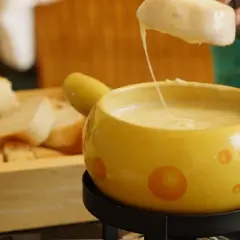 Un pezzo di pane viene intinto in una fonduta di pecorino fumante, servita in una ciotola gialla decorata.