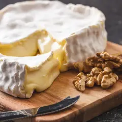 Un pezzo di brie, un formaggio grasso, su un tagliere con noci e un coltello.
