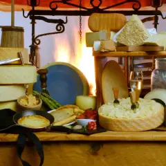 Varietà di formaggi pasta semidura, tra cui forme intere e pezzi tagliati, con uva, fragole e una padella con tortino.