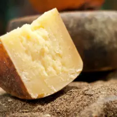 Un pezzo di formaggio sardo stagionato, con crosta scura e pasta gialla, riposa su un letto di spezie macinate.