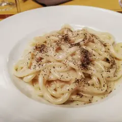 Pici cacio e pepe cremosi e fumanti, un classico della cucina romana, serviti su un piatto bianco.