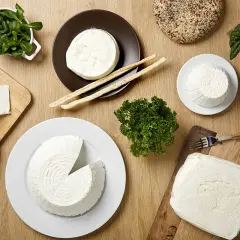 Vari tipi di formaggio fresco, tra cui lo squacquerone, un formaggio grasso, con pane, grissini e verdure su un tavolo di legno.