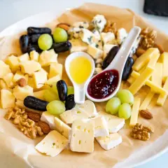 Un tagliere ricco di formaggio semistagionato, uva, noci, mandorle, miele e marmellata.
