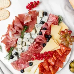 Un invitante piatto di formaggi con salumi, uva, olive e pane croccante, perfetto per un aperitivo.