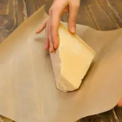 Mani che avvolgono un pezzo di formaggio stagionato nella carta forno, un metodo per conservare il formaggio al meglio.