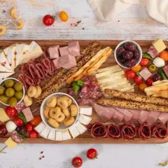 Un ricco antipasto salumi e formaggi su tagliere: salame, prosciutto, brie, taralli, olive e pomodorini.