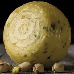 Formaggio pecorino al pistacchio, con alcuni pistacchi sparsi sul tavolo di legno.