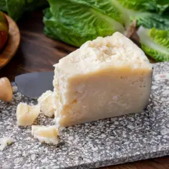 Un pezzo di pecorino siciliano stagionato, pronto per essere gustato con pomodori e lattuga fresca.