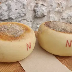 Due forme di pecorino semistagionato, con la crosta marcata e la lettera "N" rossa dipinta sul fianco, riposano su un tagliere di legno.