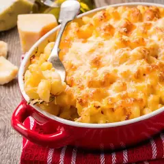 Mac and cheese dorato e filante in una teglia rossa, con pezzi di formaggio e una forchetta pronta a servirlo.