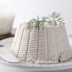 Ricotta fresca su piatto bianco, guarnita con aneto. La sua consistenza soffice rivela cosa contiene la ricotta: pura bontà.