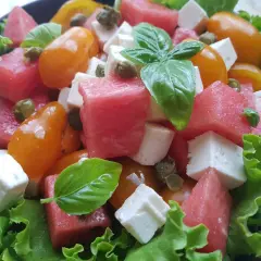 Insalata estiva con cubetti di formaggio di capra, anguria, pomodorini gialli, capperi e basilico fresco su letto di lattuga croccante.