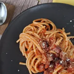 Un piatto di pasta all'amatriciana fumante, con guanciale croccante e pecorino grattugiato, pronto per essere gustato.