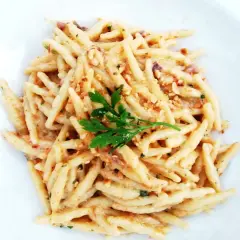 Un piatto di trofie cacio e pepe, condite con una cremosa salsa al formaggio e pepe, guarnite con prezzemolo fresco.