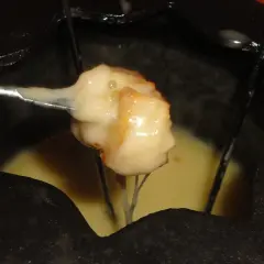Un pezzo di pane intinto nella fonduta savoyarde ricetta, filante e dorato, pronto per essere gustato.
