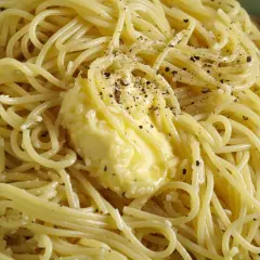Un piatto di spaghetti fumanti, conditi con burro fuso e pepe nero macinato, pronti per essere gustati come un classico cacio e pepe.