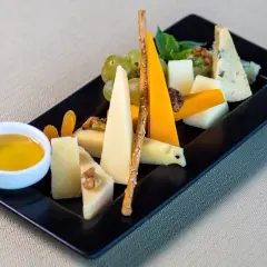 Piatto nero con vari formaggi, uva, noci, albicocche secche, grissini e una ciotolina di miele. Perfetti abbinamenti formaggi e frutta per un aperitivo.
