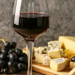 Un bicchiere di vino rosso accompagna un invitante tagliere di formaggi misti, con uva nera e un coltello da formaggio.
