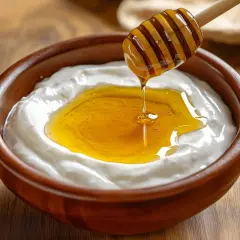 Un cucchiaio di miele cola su uno yogurt cremoso in una ciotola di legno. Attenzione, yogurt e miele fa ingrassare se consumati in eccesso!