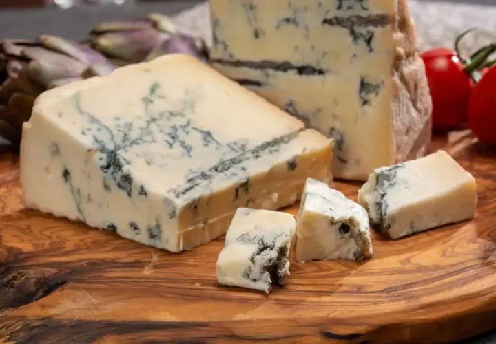 Pezzi di gorgonzola su tagliere di legno, con carciofi e pomodorini. Un assaggio dell'autentica gorgonzola origine.