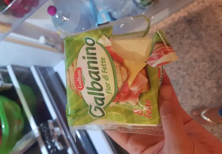 Una mano tiene una confezione di Galbanino Fior di Fette, con prosciutto e formaggio visibili. Perfetto per uno spuntino in gravidanza.