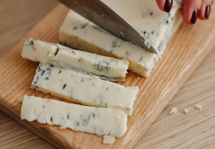 Un pezzo di gorgonzola viene affettato su un tagliere. Un desiderio di gorgonzola in gravidanza, magari per un aperitivo speciale.