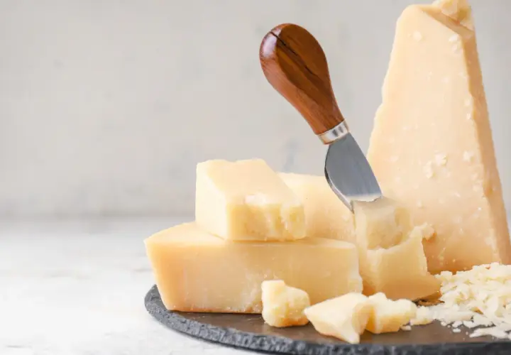 Pezzi di parmigiano reggiano, alcuni grattugiati, con un coltello. Attenzione, il parmigiano contiene lattosio.