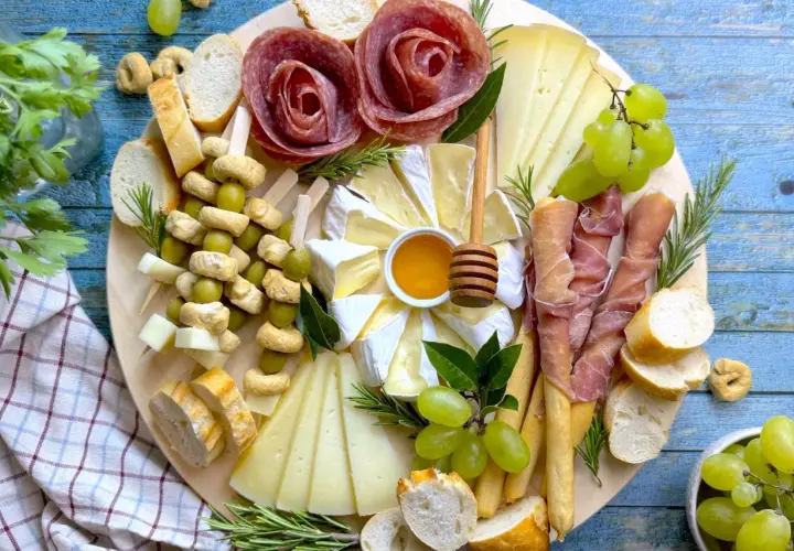 Un vassoio con formaggi, salumi a rosa, uva, olive e pane. Ecco come disporre i salumi nel piatto per un antipasto invitante.