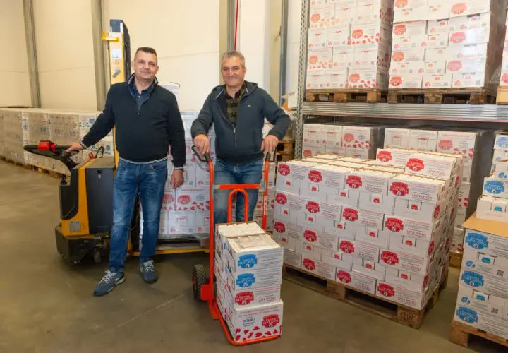 Due uomini in un magazzino con scatoloni di latte a lunga conservazione aperto fuori dal frigo.
